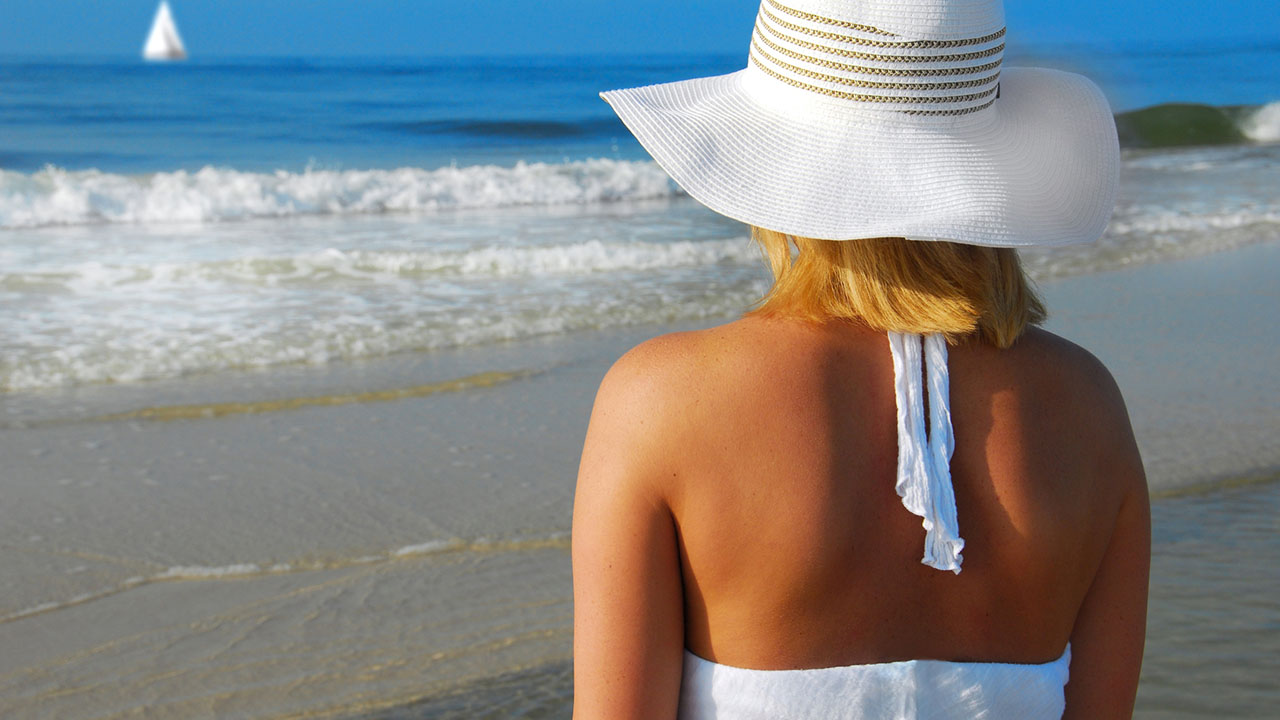 Woman on beach looks out at sailboat